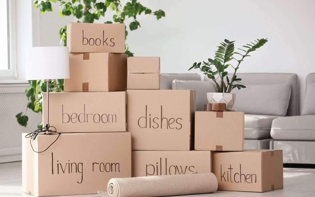 Labeled moving boxes for books, dishes, bedroom, and kitchen stacked in a bright living room