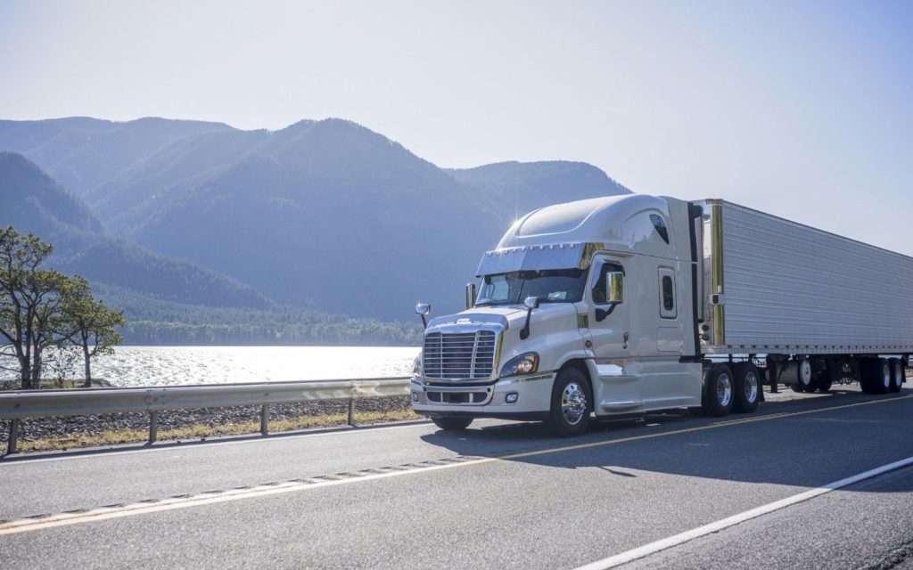A moving truck traveling down a road with mountains in the background.